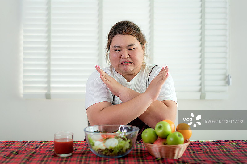 亚洲超重女性出于对健康、营养、减肥、生活方式、健康食品和节食理念的考虑，对情绪厌倦而拒绝食用餐桌上的新鲜绿色蔬菜沙拉图片素材