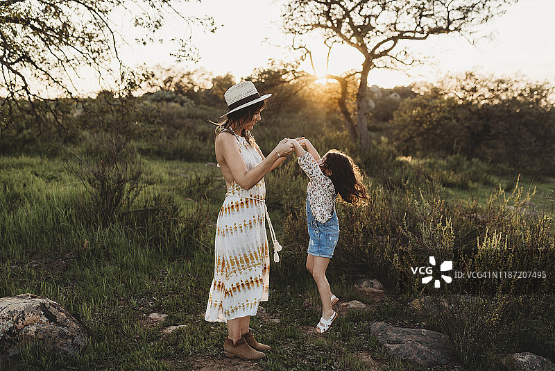 年轻的母亲和女儿在阳光明媚的草地上跳跃的全景图片素材