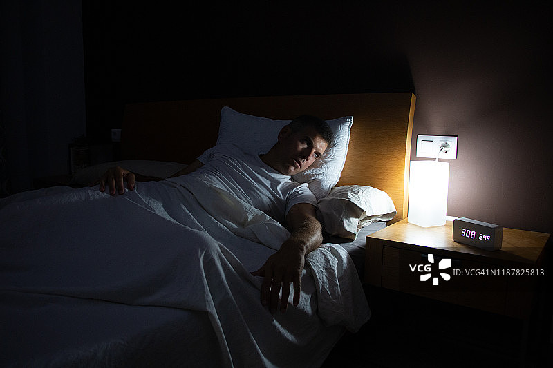 一个失眠的人在黎明时分从床上关切地看着时钟图片素材