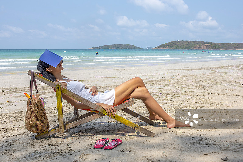 年轻女子在沙滩上看书放松。图片素材