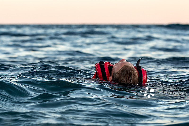 黄昏时分，在公海上，身穿救生衣的奄奄一息的溺水女孩图片素材