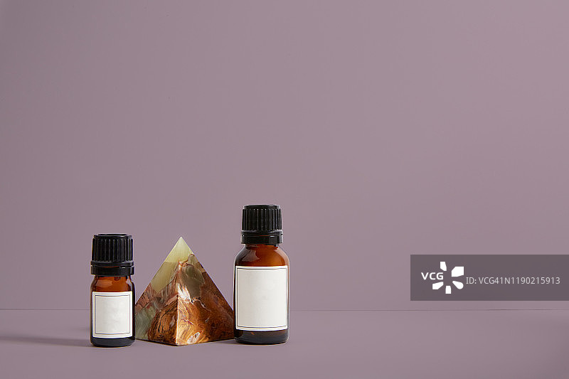 贴着白色标签的棕色小瓶子紧挨着科亚米托玛瑙金字塔，坐落在粉红色的田野上。图片素材