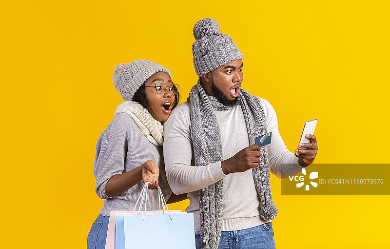 一对惊讶的黑人夫妇看着智能手机，在网上购物图片素材