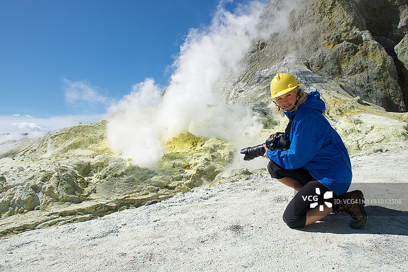 一位微笑的女士正在拍摄新西兰丰饶湾北岛的怀特岛火山图片素材