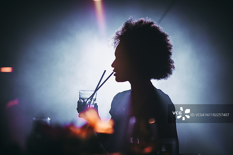 一个女孩的剪影与一个非洲发型在一个夜总会喝鸡尾酒图片素材