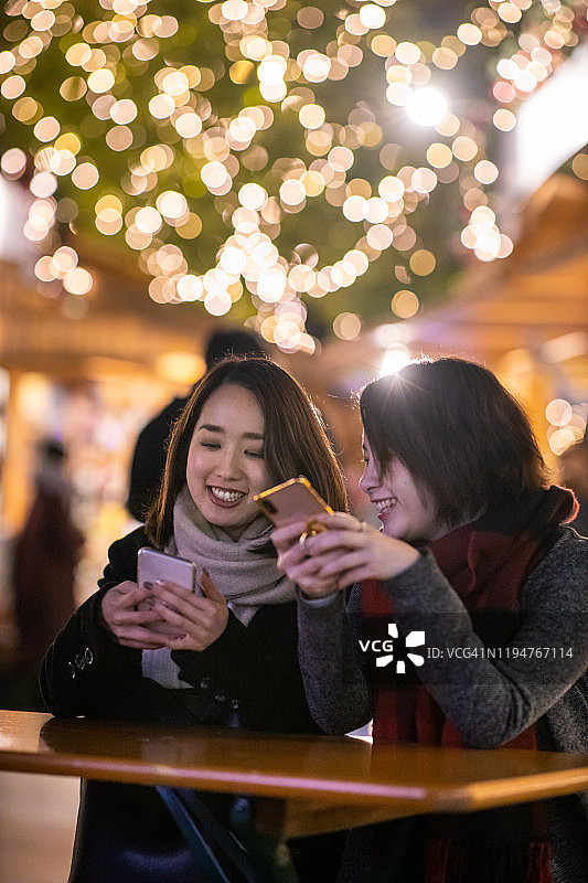 年轻女性朋友在圣诞市场使用智能手机图片素材