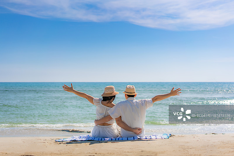 幸福的亚洲夫妇举起手臂显示幸福和乐趣的天堂海滩与完美的原始绿松石水在阳光明媚的热带度假。夏季旅行和自由的海滩度假。图片素材