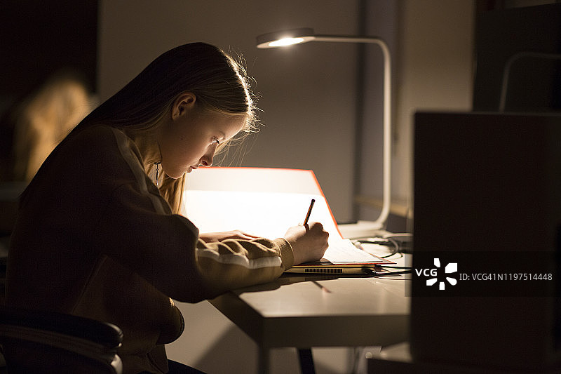 女孩(12-13岁)晚上在台灯下做作业图片素材