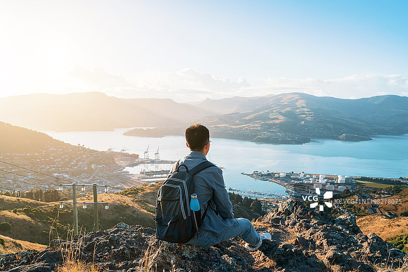 一位年轻的亚洲男子在新西兰的山顶上欣赏美丽的自然景观图片素材