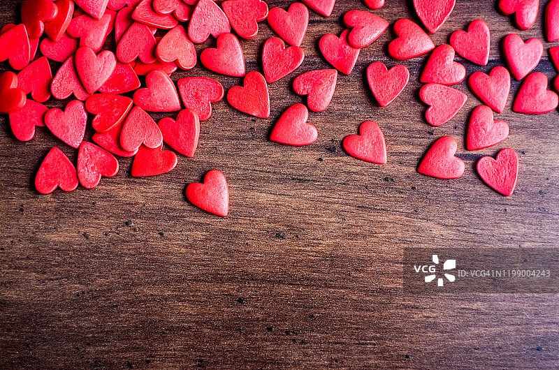 情人节背景与红心木桌子上，俯视图。红色的心型糖果在木制的棕色背景上。情人节的概念。图片素材