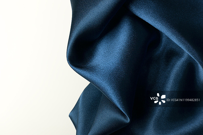 一个豪华的蓝色织物的抽象背景波浪形褶皱丝绸质地的缎子材料上的白色背景。经典蓝色豪华背景与复制空间。图片素材
