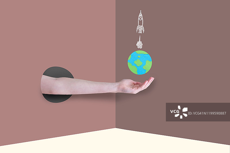 一只从墙上的一个洞里伸出来的手臂，手上拿着一个世界地球仪和火箭飞船。图片素材