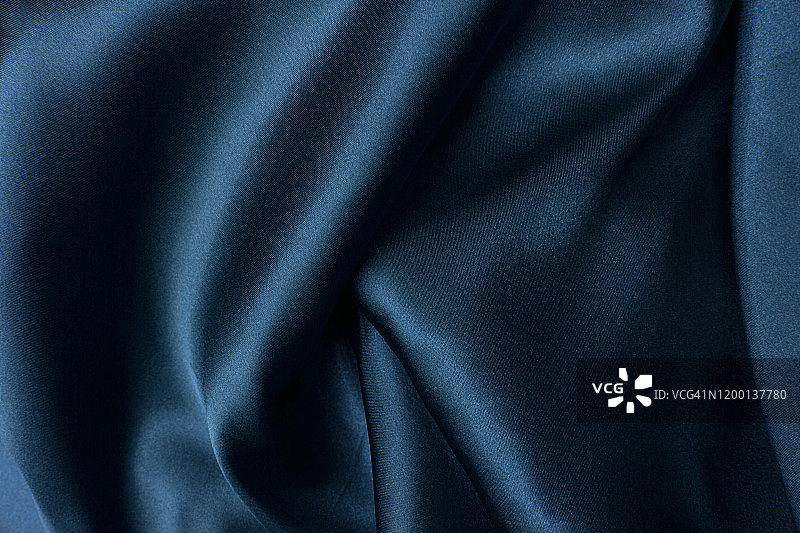 波浪褶皱的蓝色丝绸纹理缎子天鹅绒材料或豪华的蓝色丝绸作为背景，褶皱的蓝色丝绸织物。图片素材