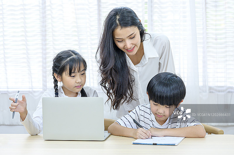亚洲母亲或女教师帮助女孩和男孩做家庭作业。人、学、育的观念。图片素材