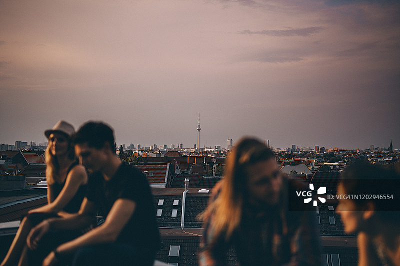 黄昏时分，在城市的屋顶聚会上，朋友们坐在露台上聊天图片素材