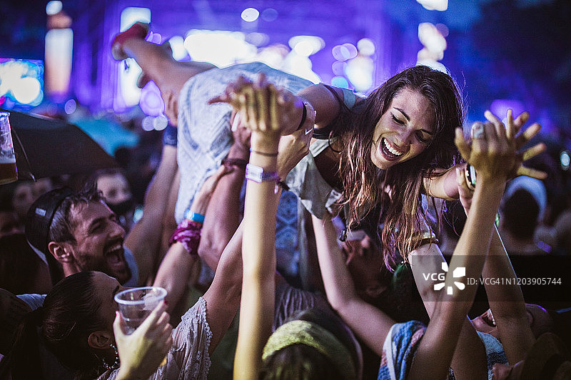 一个年轻开朗的女人在音乐节的夜晚被她的朋友抱着。图片素材