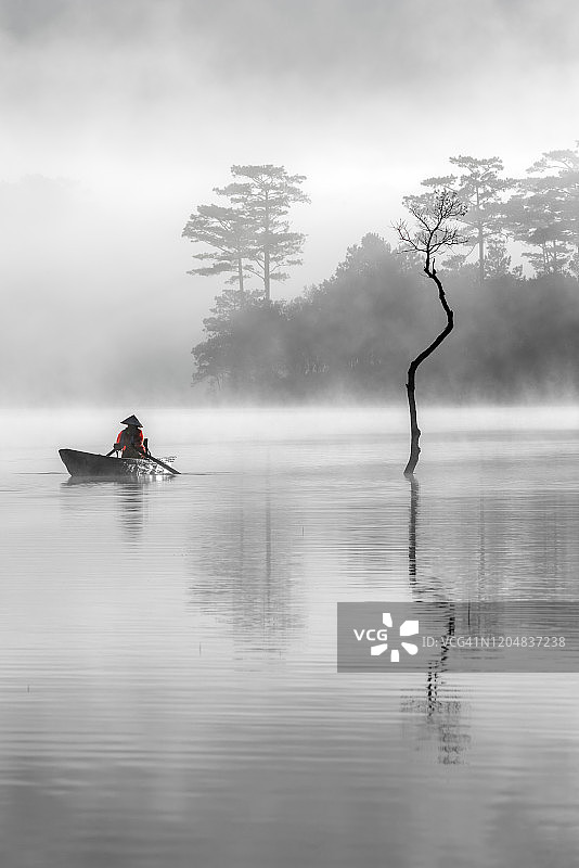 戏剧性的风景与孤独的渔民和树反射在雾湖，照片的单色版本图片素材