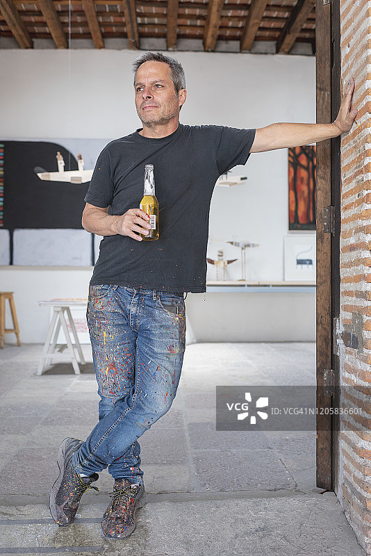 一个喝啤酒的艺术家靠在他工作室的门口图片素材