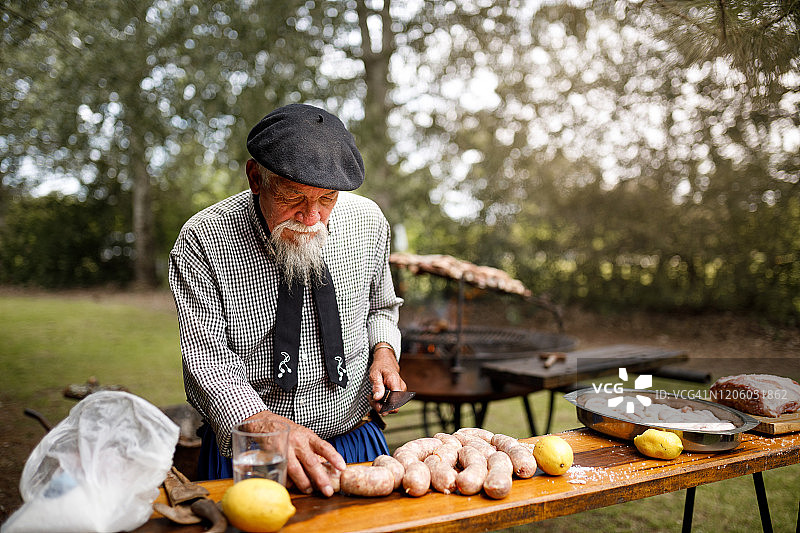 一个老男人在乡下房子的花园里切猪肉香肠图片素材