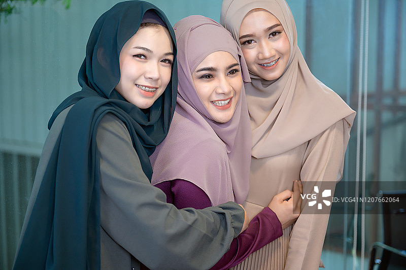 两个穆斯林女性朋友戴着头巾愉快地拥抱着，看着镜头，拥抱着对方。友谊的概念永远的股票照片图片素材