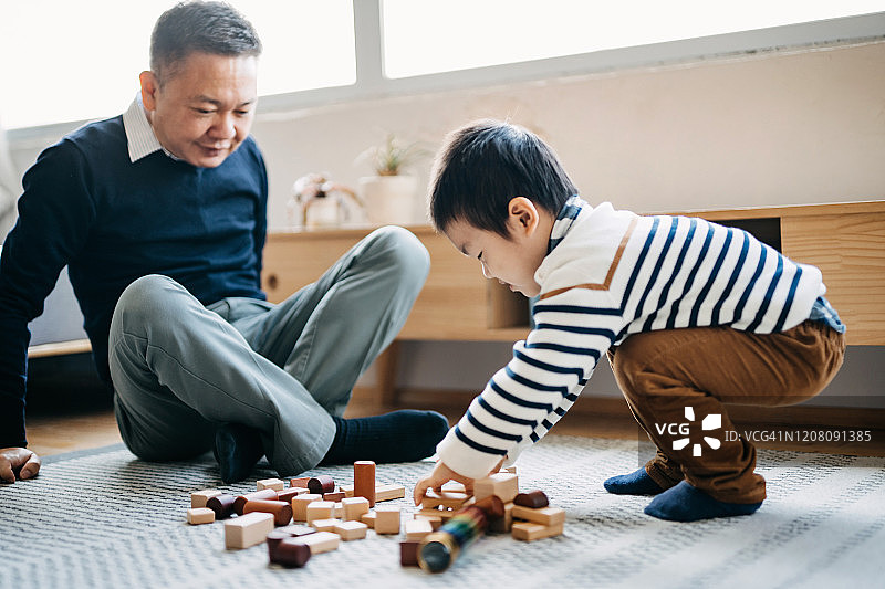 快乐的亚洲爷爷坐在客厅的地板上和小孙子一起玩积木图片素材