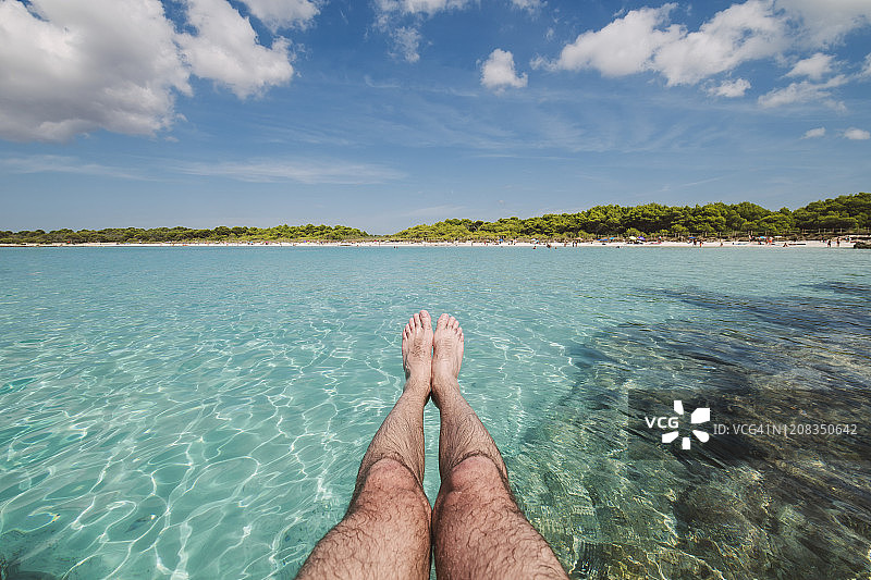 一个男人的腿在sonsaura海滩前，Menorca，西班牙。图片素材