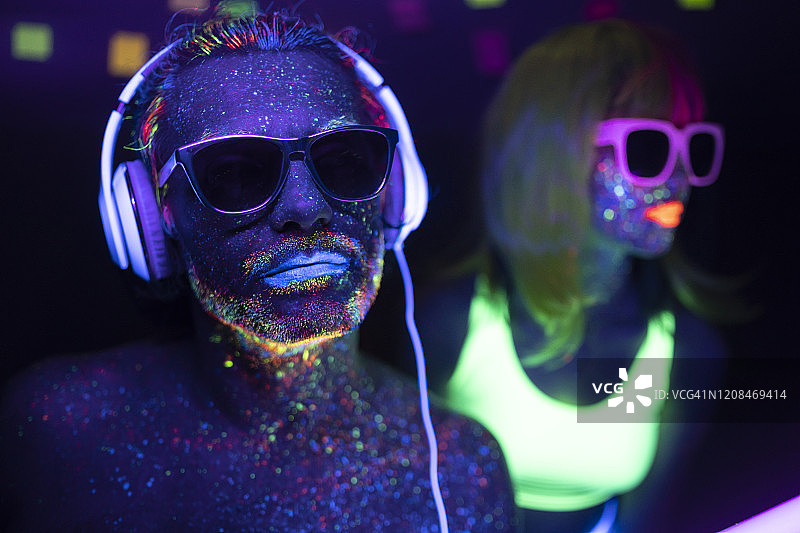 一对戴着太阳眼镜涂着荧光紫外线的夫妇，戴着耳机的男人图片素材
