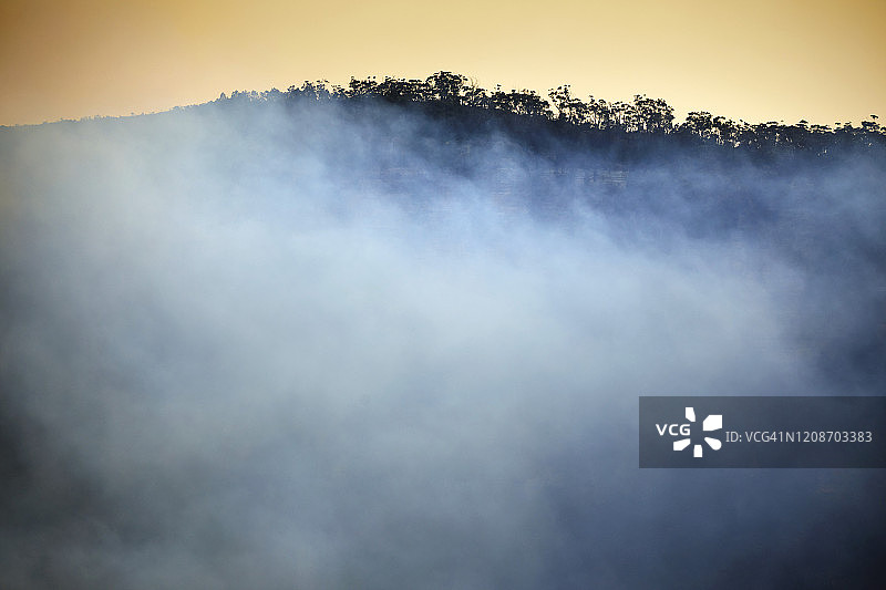 烟雾在山谷从森林火灾与树木成行的山脊图片素材