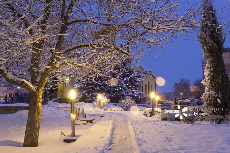 从圣三一大教堂的公园区域可以看到白雪皑皑的冷杉树和寺庙。在黎明前的黑暗中，灯笼和花环的灯光图片素材