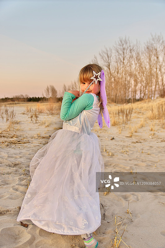一个可爱的小女孩打扮成仙女在日落的海滩上的肖像图片素材