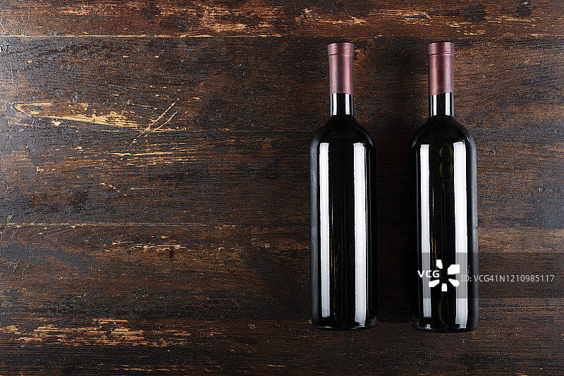 棕色的木制背景上放着两瓶紧闭的葡萄酒。文本。图片素材