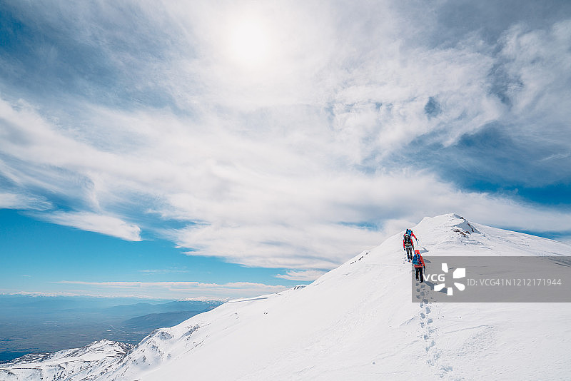冬季高山登山队在高海拔的山峰上排成一行行走图片素材