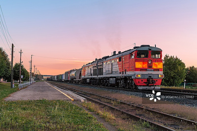 强大的柴油机车和沉重的货运列车在美丽的夕阳下图片素材