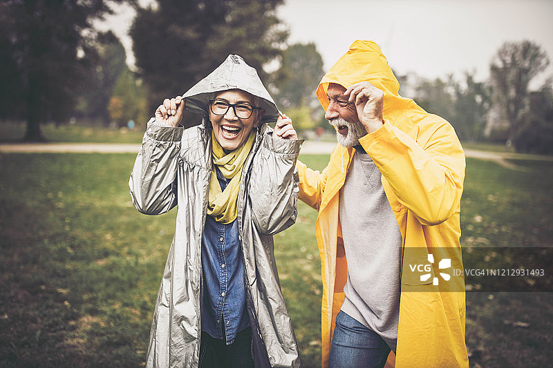 快乐的老年夫妇在雨天的大自然中穿着雨衣。图片素材