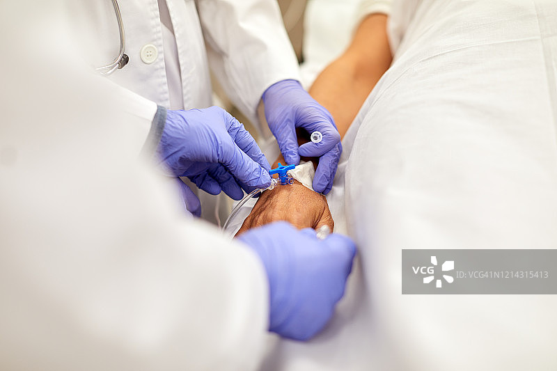 一个医生和护士应用静脉滴注病人的近视图。图片素材