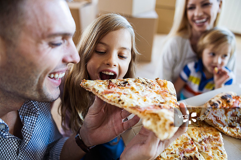 快乐的爸爸和女儿在搬进新家后吃披萨午餐。图片素材