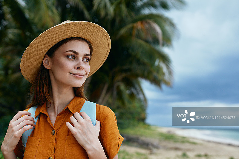 在热带植被和海洋的背景下，一名年轻女子背起背包背带，把目光移开图片素材