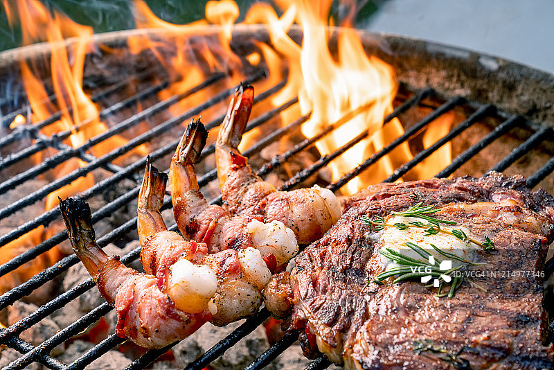 美味的肋眼牛排和培根卷虾在燃烧的热烧烤图片素材