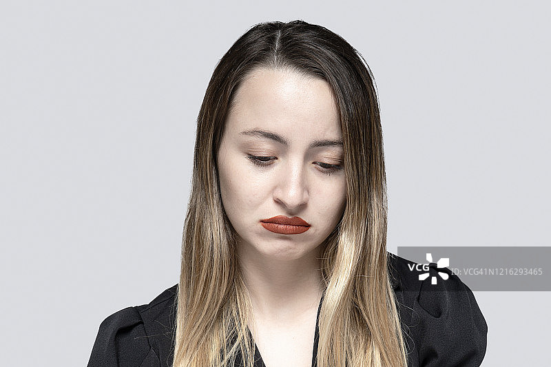 悲伤的年轻女子肖像与沮丧的面部表情在灰色的背景图片素材
