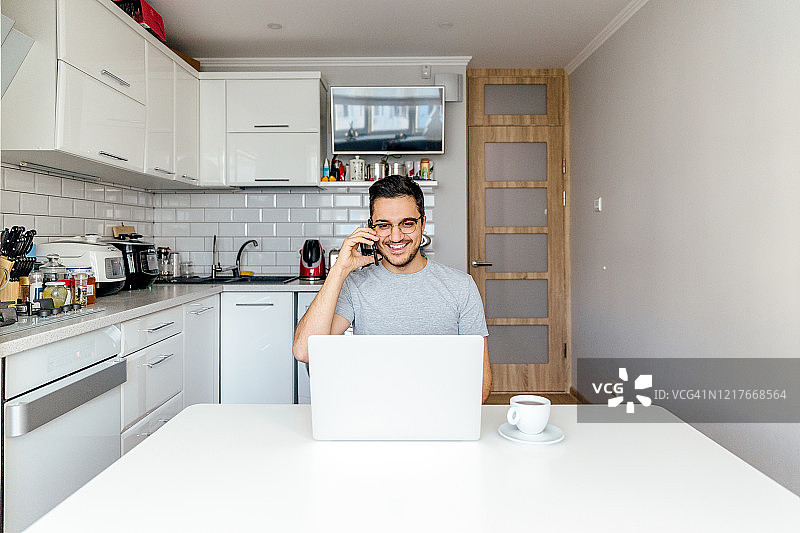 一个年轻人在家厨房用笔记本电脑工作图片素材