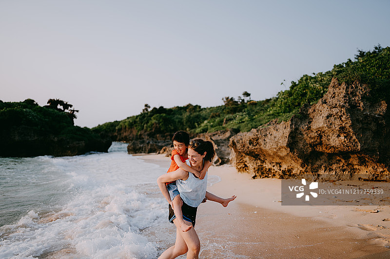 在日本冲绳的海滩上，妈妈背着她的小女孩图片素材