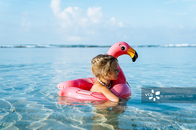 可爱的金发小女孩和粉红色的充气火烈鸟游泳在热带海洋的暑假。图片素材