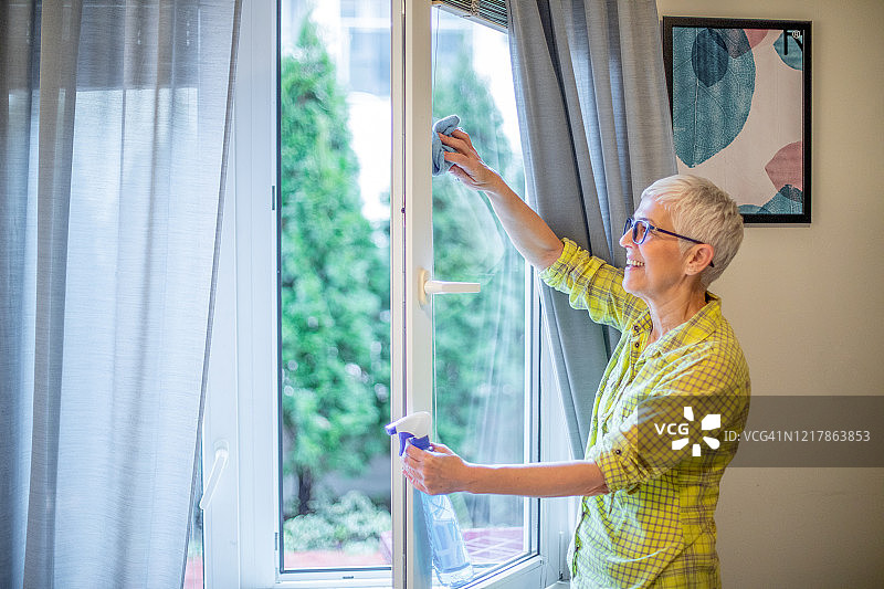 快乐的老年成熟的家庭主妇在洗窗户。图片素材