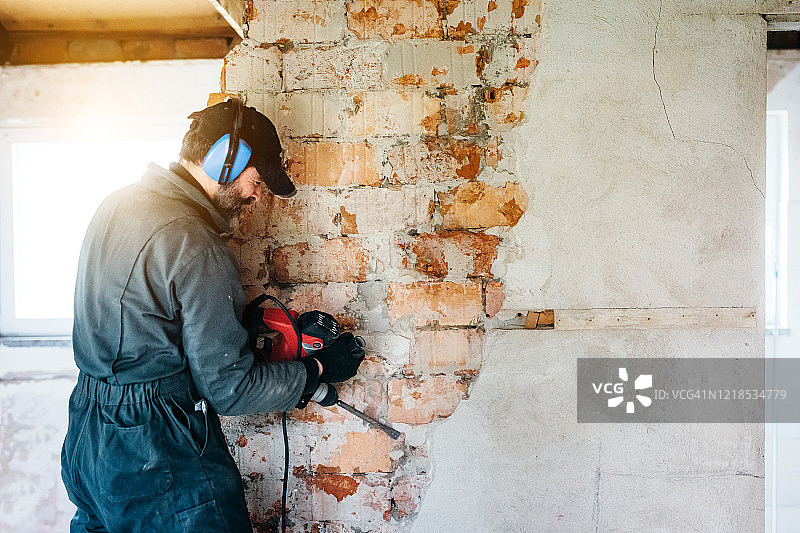 成熟的工人用钻机拆除房子里的墙壁图片素材