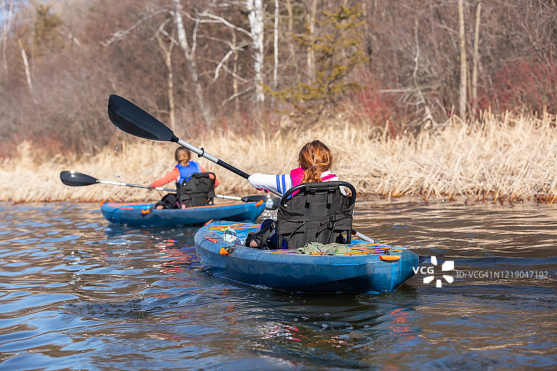 两个年轻的女孩在初春的湖上皮划艇图片素材