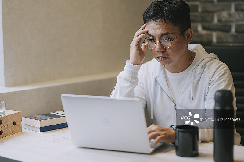 一个亚洲华人中年男子专注于网上工作，用他的笔记本电脑输入商业计划书并回复电子邮件图片素材