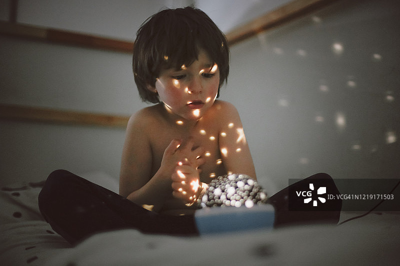 男孩坐在床上看星星灯图片素材