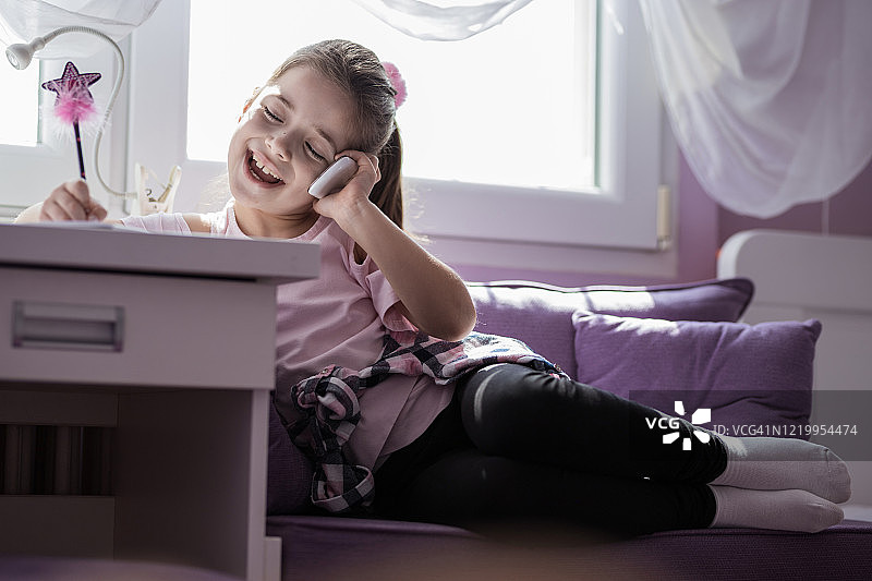 快乐的小女孩坐在窗边愉快地讲电话图片素材