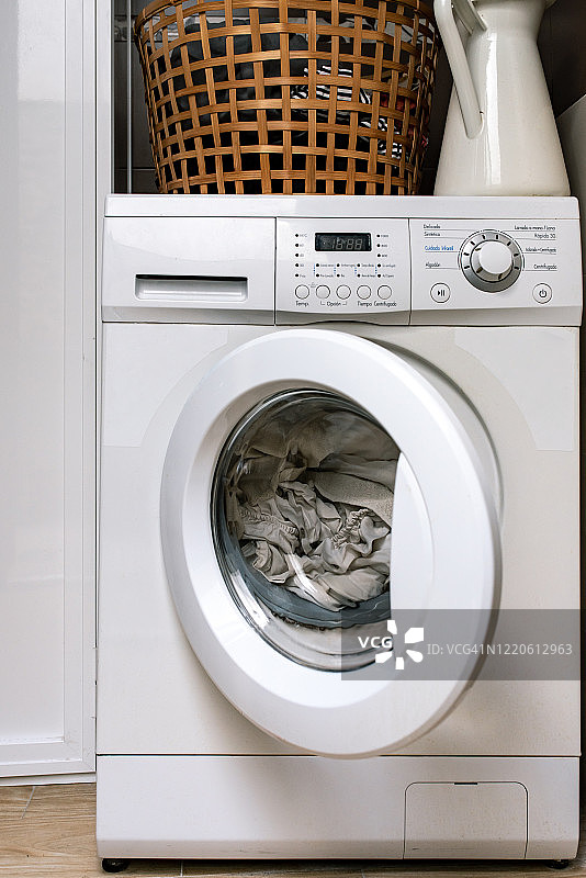 一个半开着的装满洗衣机。上面有一个篮子，里面放着要洗的衣服图片素材