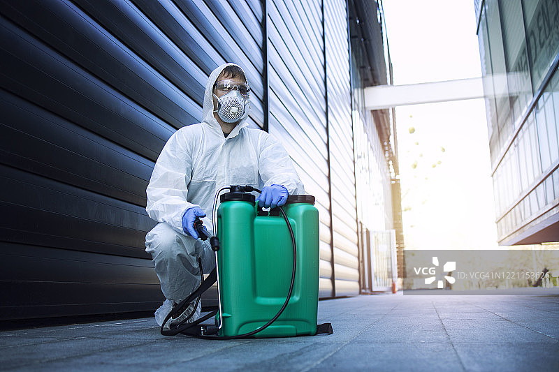城市消毒。身穿白色防护服的男子通过喷洒器在储水箱中喷洒消毒剂和化学药品，以阻止高传染性冠状病毒或COVID-19的传播。图片素材